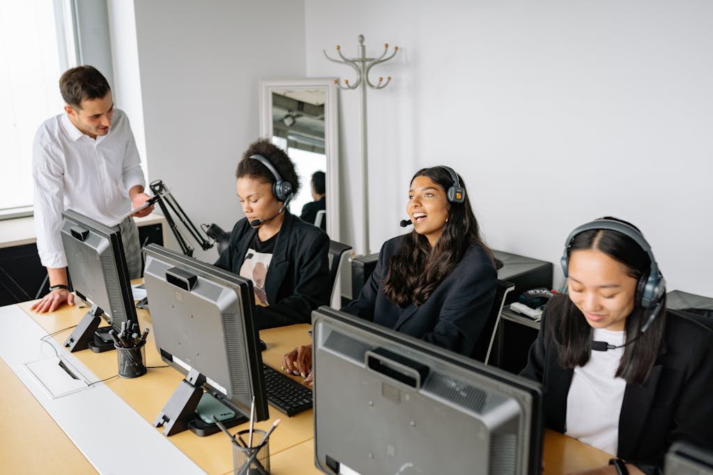 A diverse team of customer service representatives working in an office setting, wearing headsets and using computers.