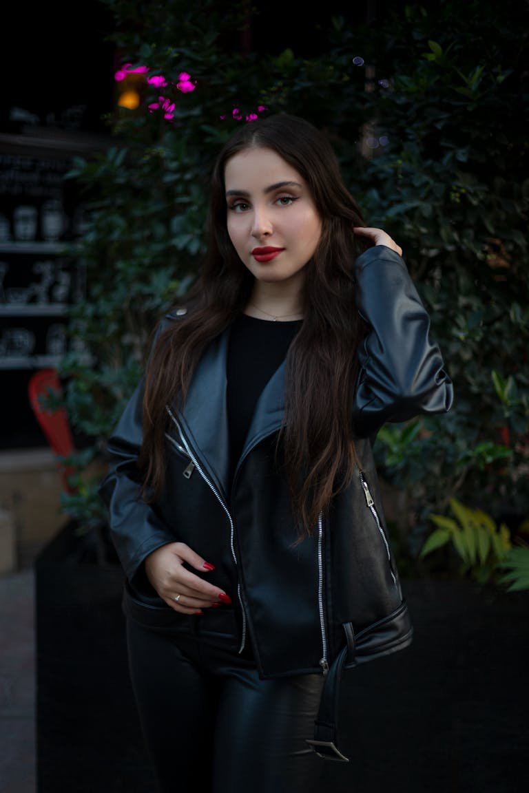 Stylish woman with red nails and leather jacket posing outdoors at night.