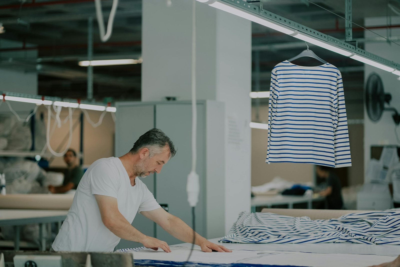 Adult male in a textile workshop working with striped fabric indoors.